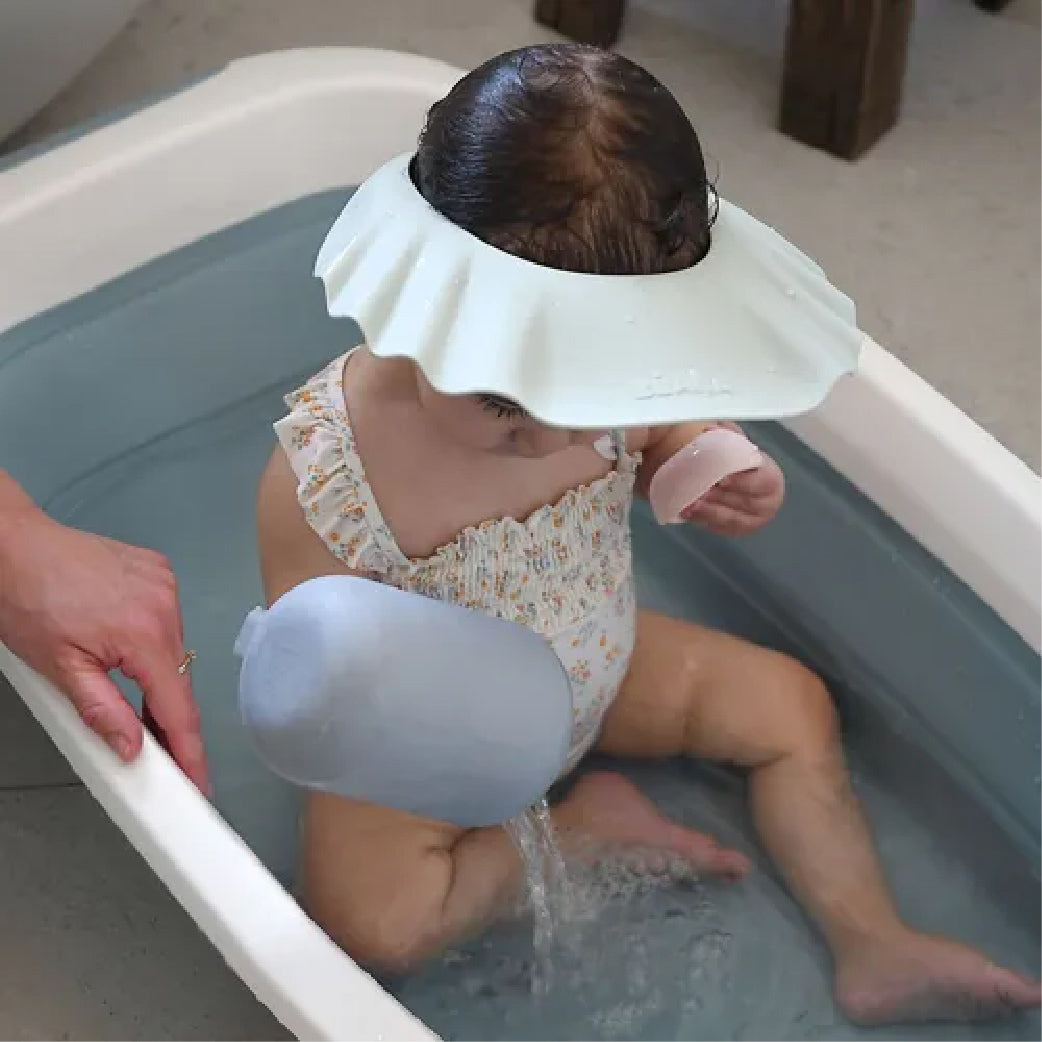 Bébé dans baignoire avec bonnet de bain anti-eau pour lavage doux des cheveux