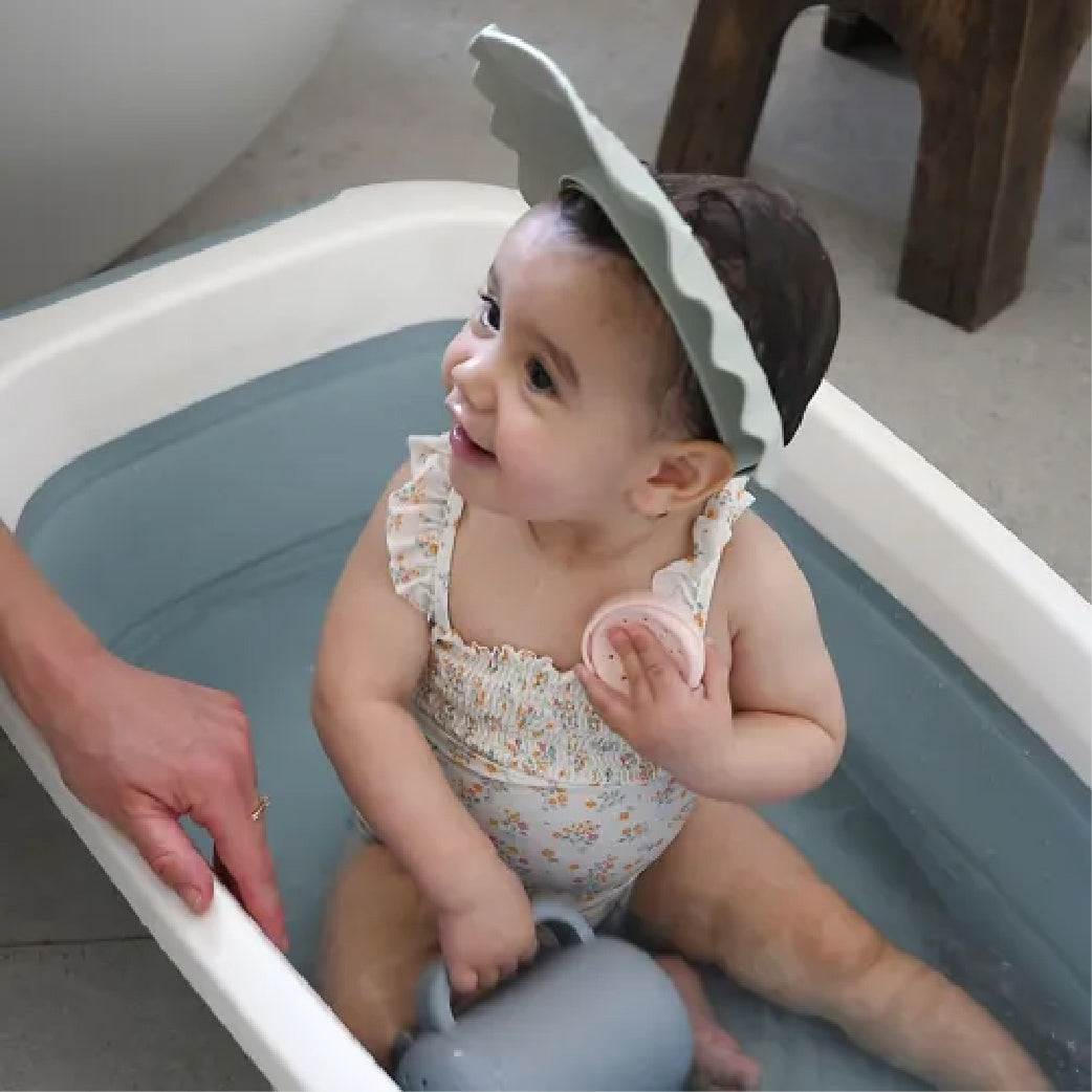Bébé souriant dans baignoire avec bandeau anti-eau, vêtement floral, jouet de bain, soin doux pour bébé