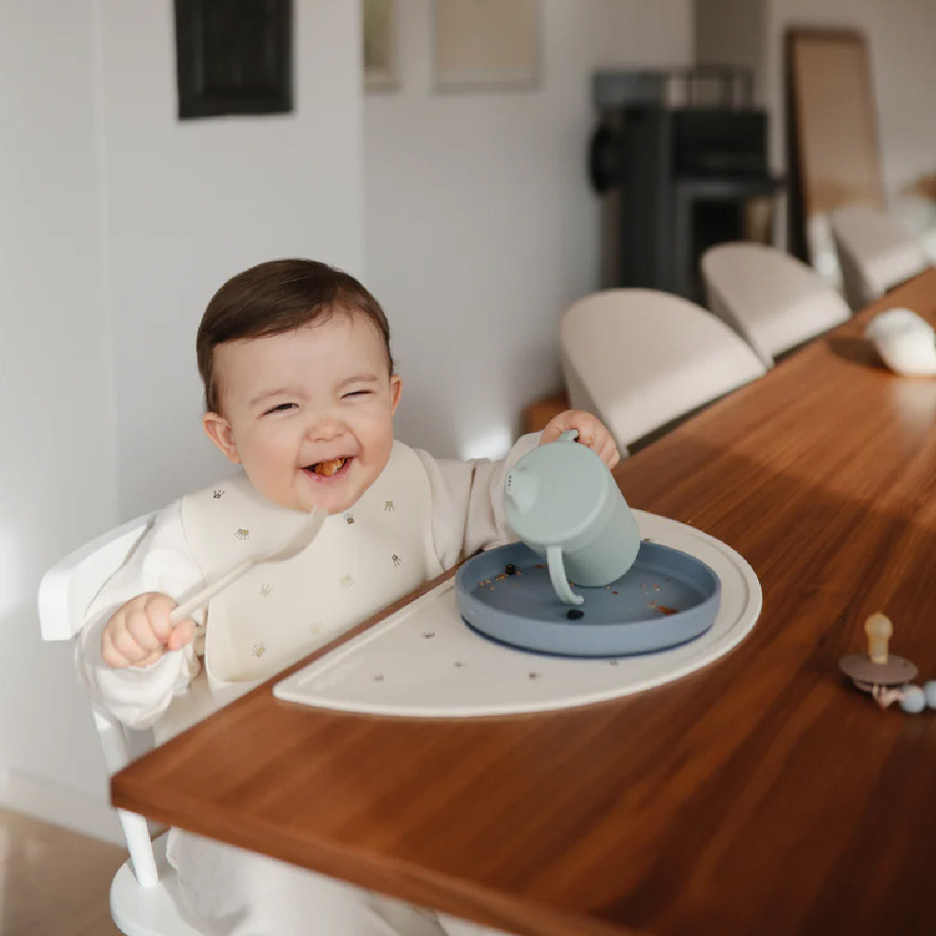 Bébé souriant en chaise haute avec assiette et gobelet anti-débordement pour repas bébé